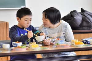 笑顔で料理を食べる親子の画像