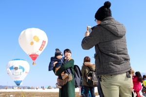 熱気球を背景に写真を撮る親子連れの画像