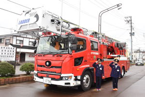 消防車の前で敬礼をする児童の画像