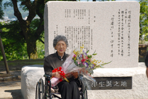 碑の前で微笑む田中志津さんの画像