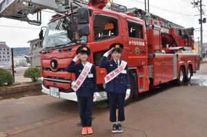 はしご車の前で敬礼をする小学生の画像