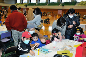 工作教室で紙飛行機を作る子どもと保護者の画像