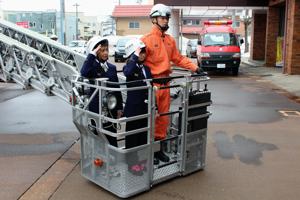 はしご車に乗って敬礼ポーズをとる一日消防署長の画像