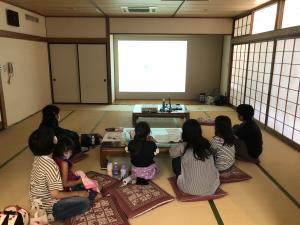 市民会館和室で壁面に投影した動画を見る子育てサークルの親子の画像